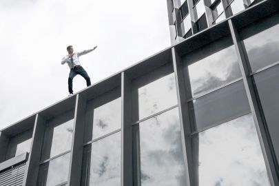 Ein junger Mann in Turnschuhen, Hemd und Krawatte steht auf einem Hochhaus in dynamischer Pose.